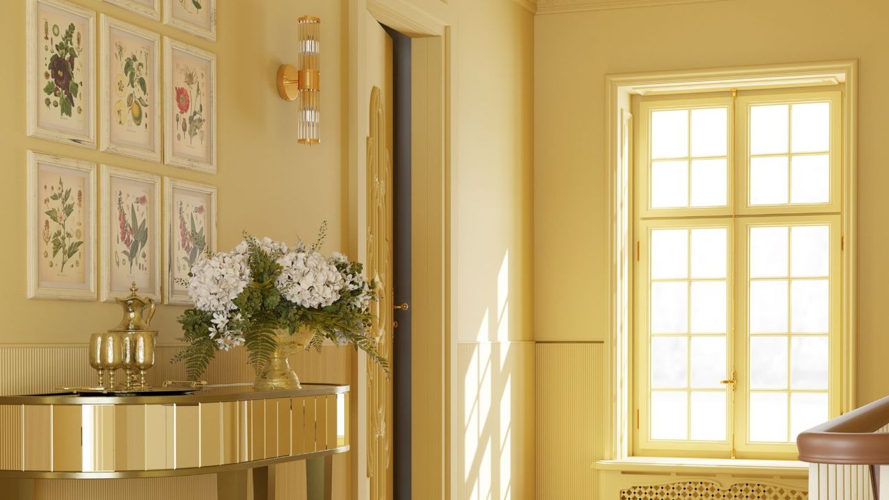 A yellow entryway with a wall with botanical prints, a gold console table, and a window