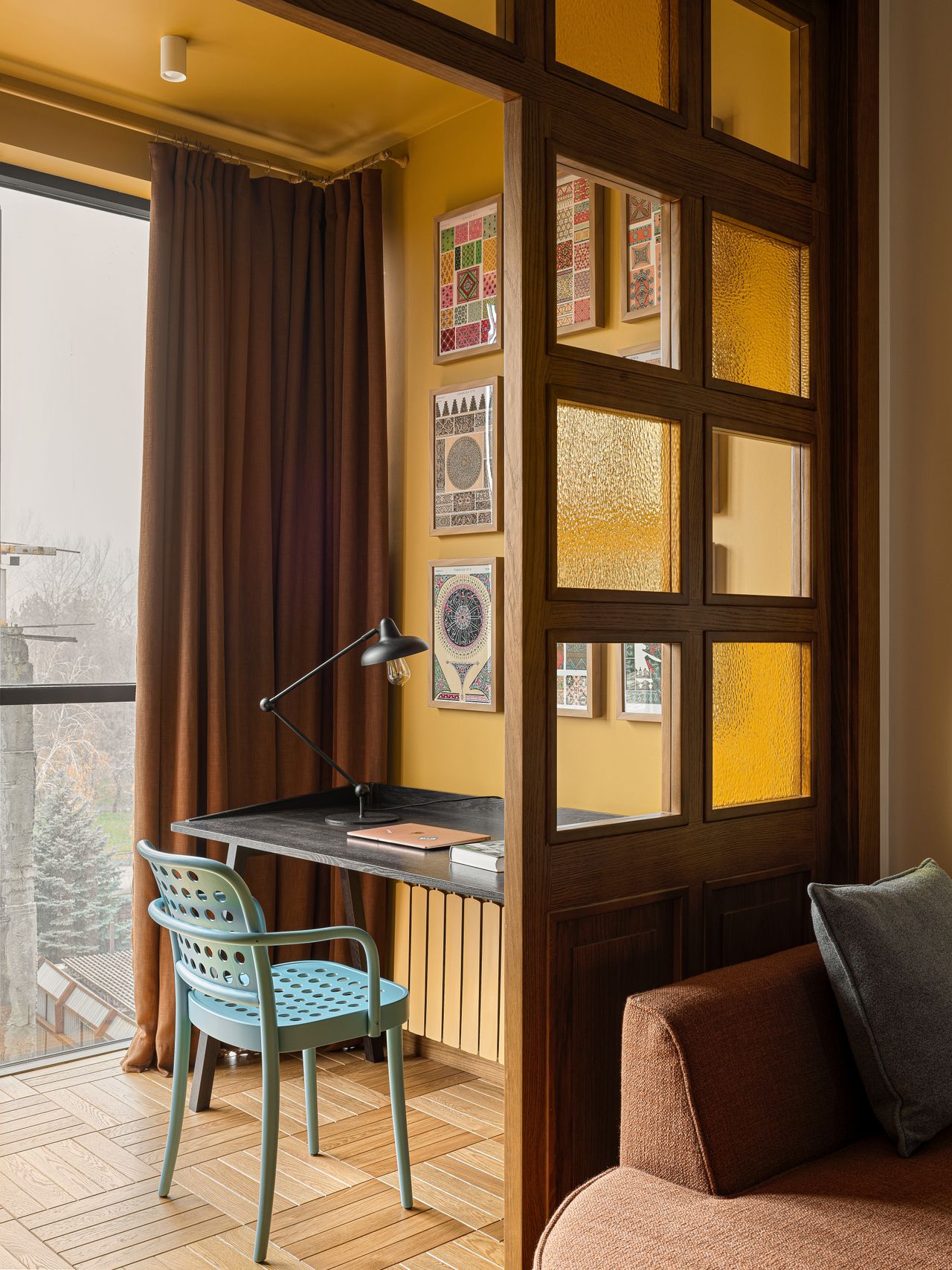 A home office situated next to the window, painted yellow, with dark toned furniture
