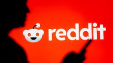 A woman looks at a smartphone with a Reddit logo displayed in the background