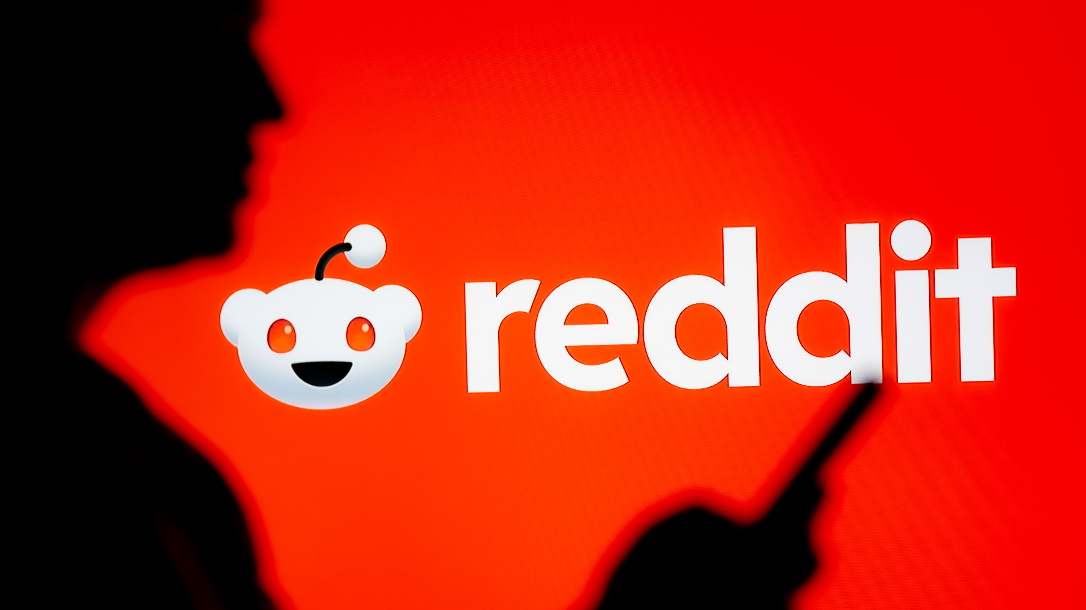A woman looks at a smartphone with a Reddit logo displayed in the background