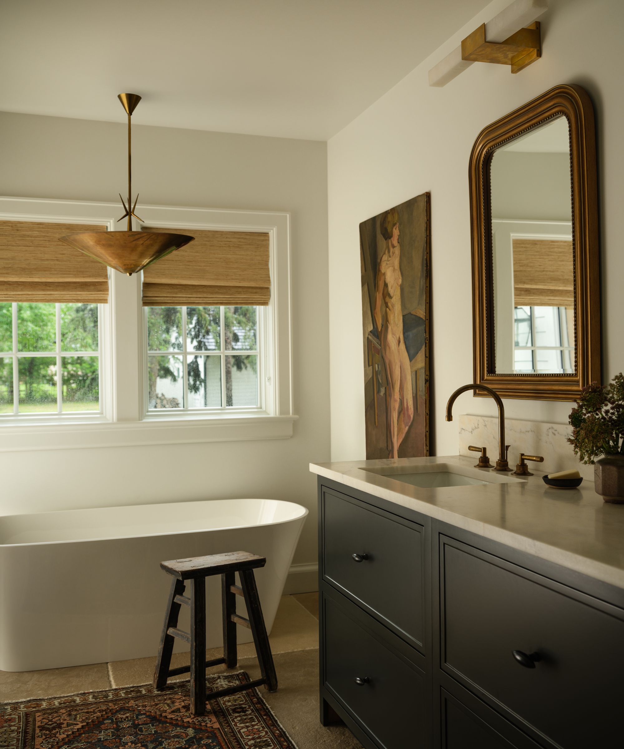 a neutral bathroom layered with antiques with a modern freestanding tub and a dark vanity