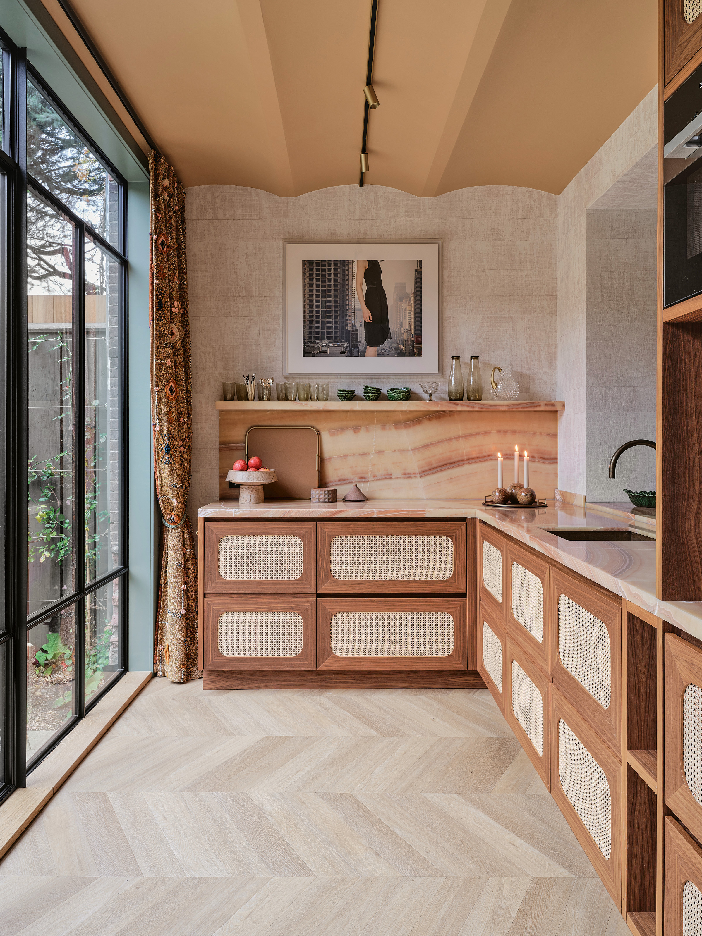 End of a kitchen with wood and cane units, peachy stone splashback and vaulted ceiling