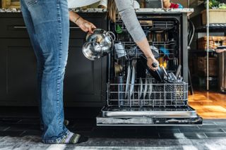 How much does a dishwasher cost to run? A woman loads a dishwasher in a dark coloured kitchen