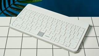 a wide picture showing all the keys on a white, lightweight tablet keyboard made by mokibo rests upon a white tiled table with a blue background