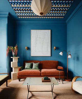 vibrant blue color drenched living room with a patterned accent ceiling and a deep velvet rust couch