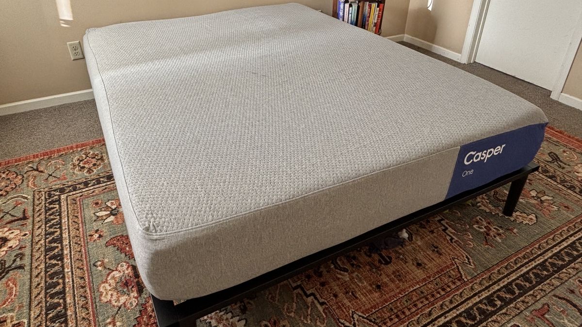 A queen-size Casper One Mattress on a black bed frame on top of an ornate bedroom rug with shades of red and green