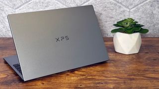A closed silver XPS laptop sits on a rustic wooden desk beside a small green succulent in a white pot, creating a calm, minimalist workspace.