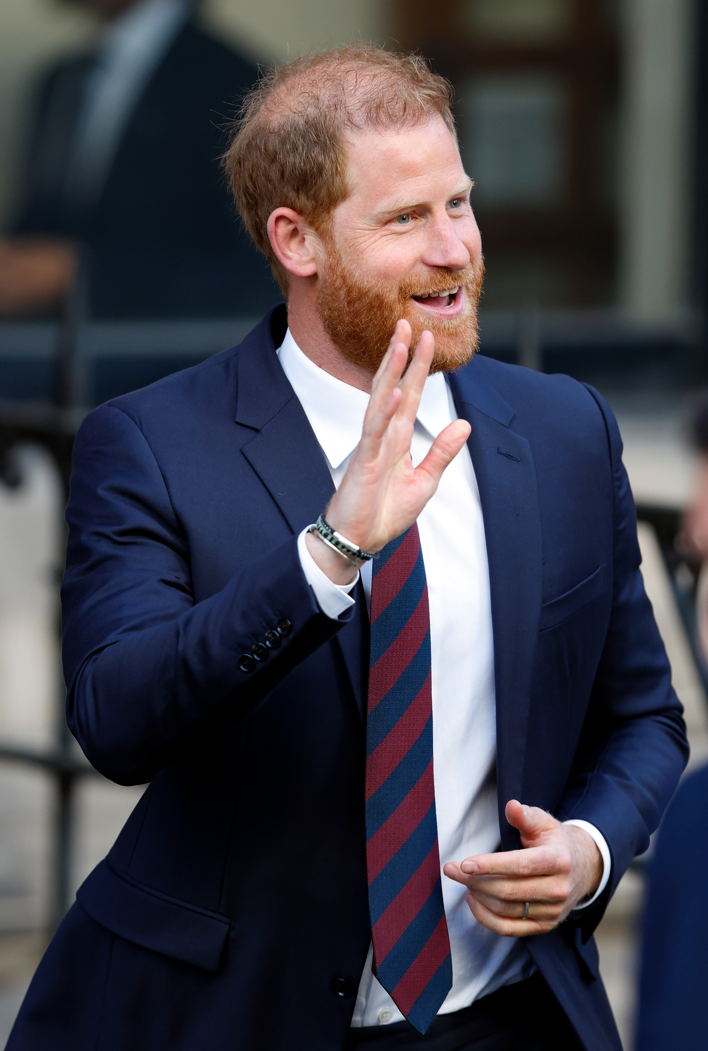 Prince Harry wearing a navy suit and waving and smiling outside court