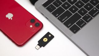 A YubiKey 5C NFC on a flat surface with an iPhone and a MacBook.