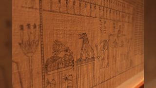 This close-up from the Book of the Dead shows a creature (with a long snout and sitting back on its hind legs like a dog,), possibly Ammit, sitting before Osiris, the Ancient Egyptian god of the underworld.