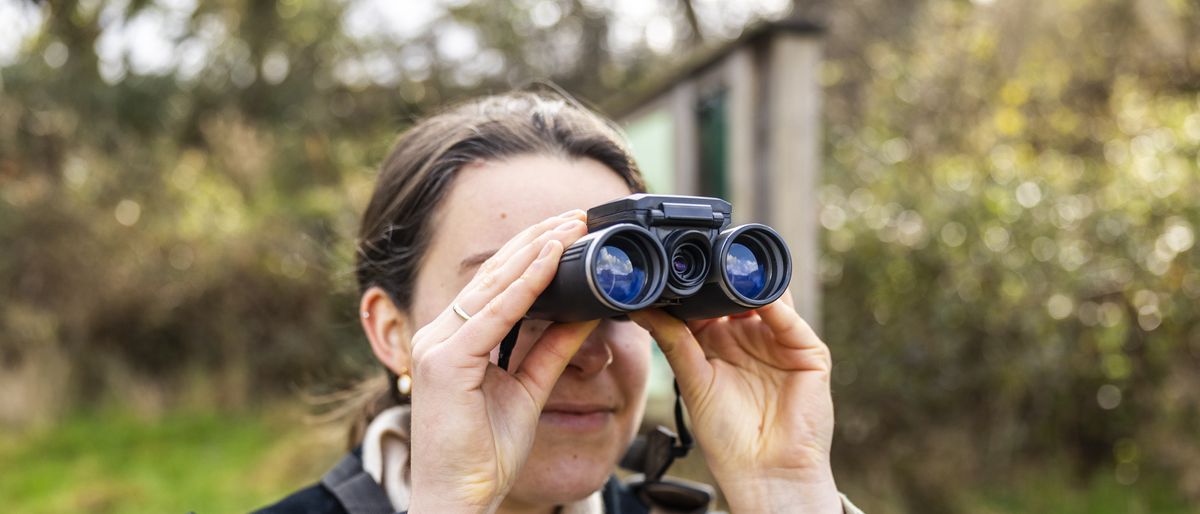 A female photographer holds the Camonity 5M 2&quot; LCD 16GB Digital Binoculars in her hands in a sunny field