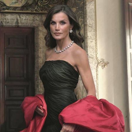 Queen Letizia wearing a black strapless gown and red stole with a huge diamond necklace standing in front of a wooden door