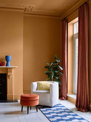 living room with orange walls, cinnamon curtains, white accent chair and fireplace