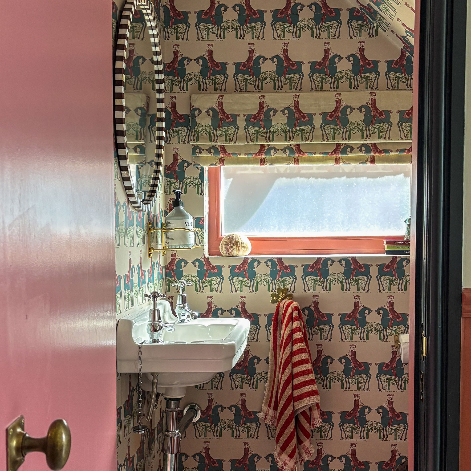 Bathroom with pink-red door and patterned wallpaper with matching window blind fabric