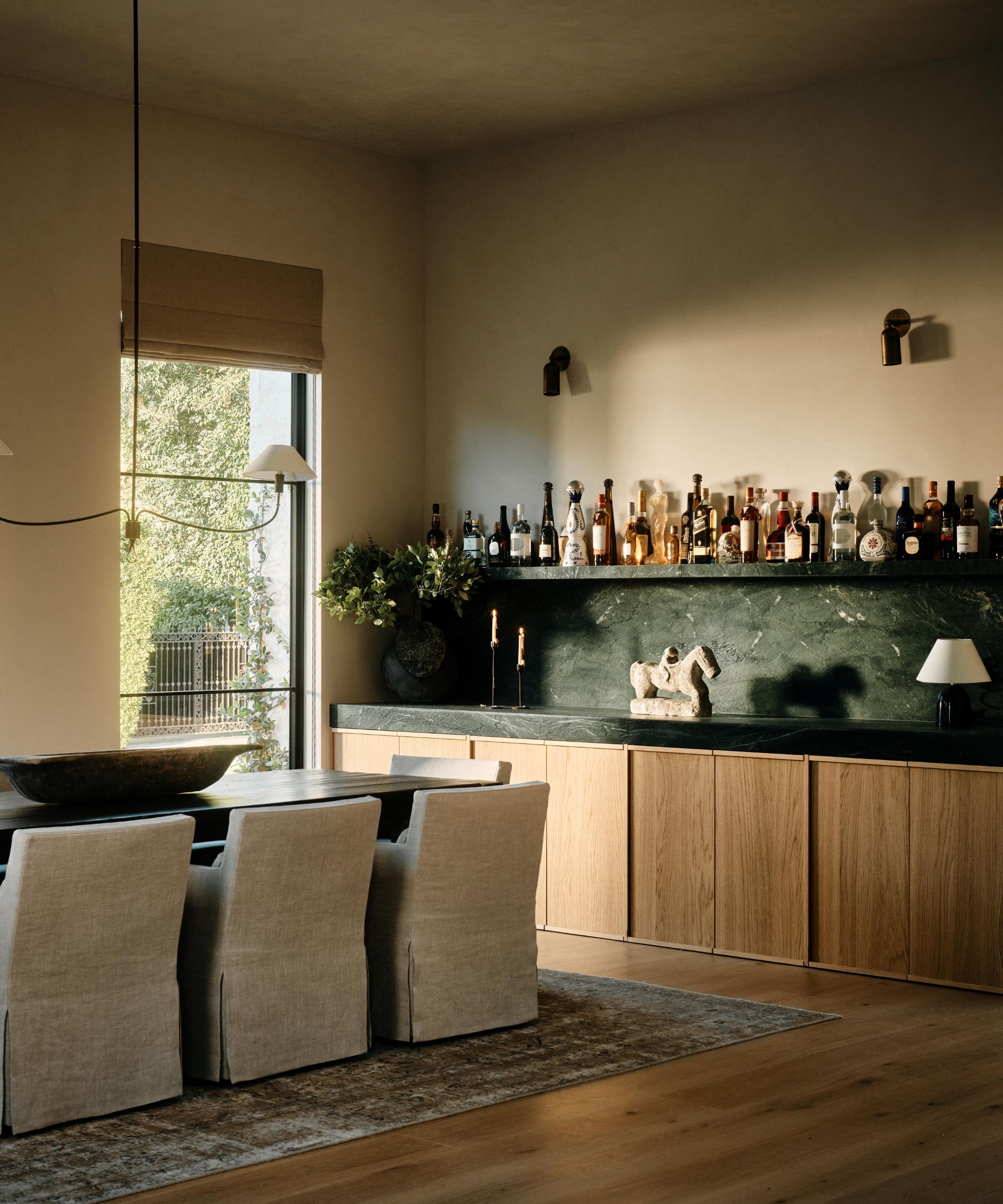 a warm greige dining room with linen slipcovered chairs and a large oak and green marble home bar