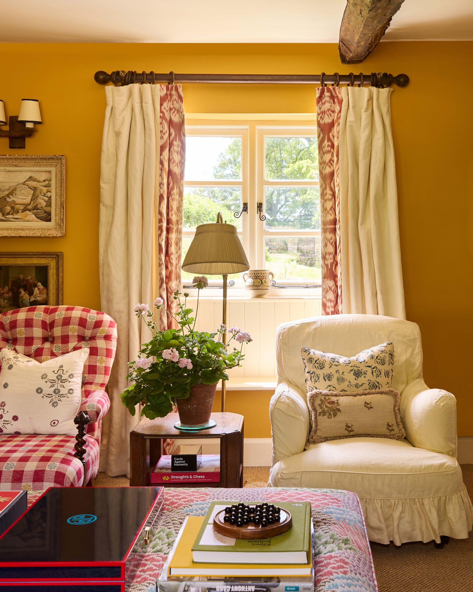 A living room painted mustard yellow with an upholstered ottoman and slipper chairs in loose covers