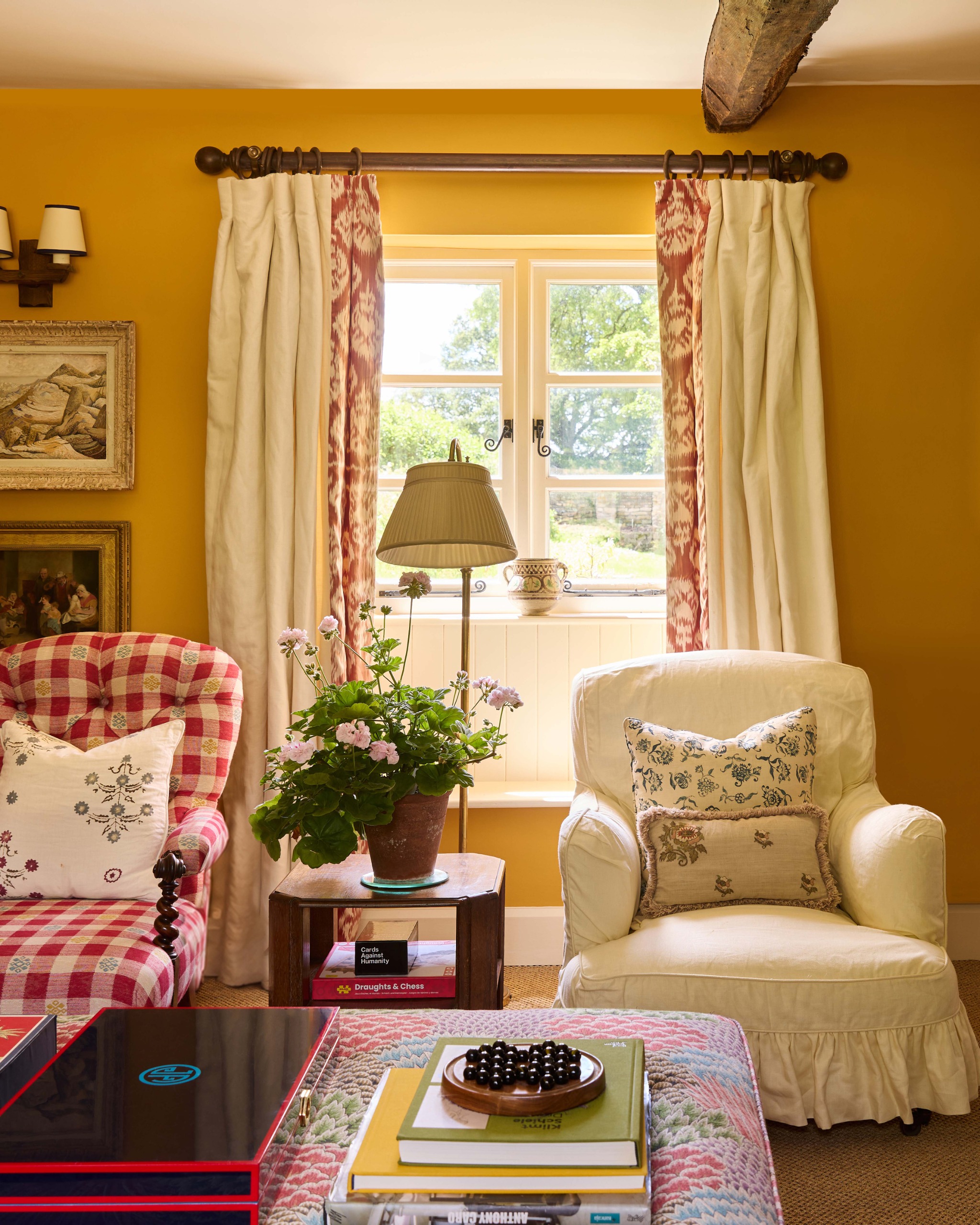 A living room painted mustard yellow with an upholstered ottoman and slipper chairs in loose covers