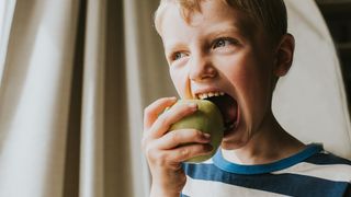 Young boy biting into a green apple