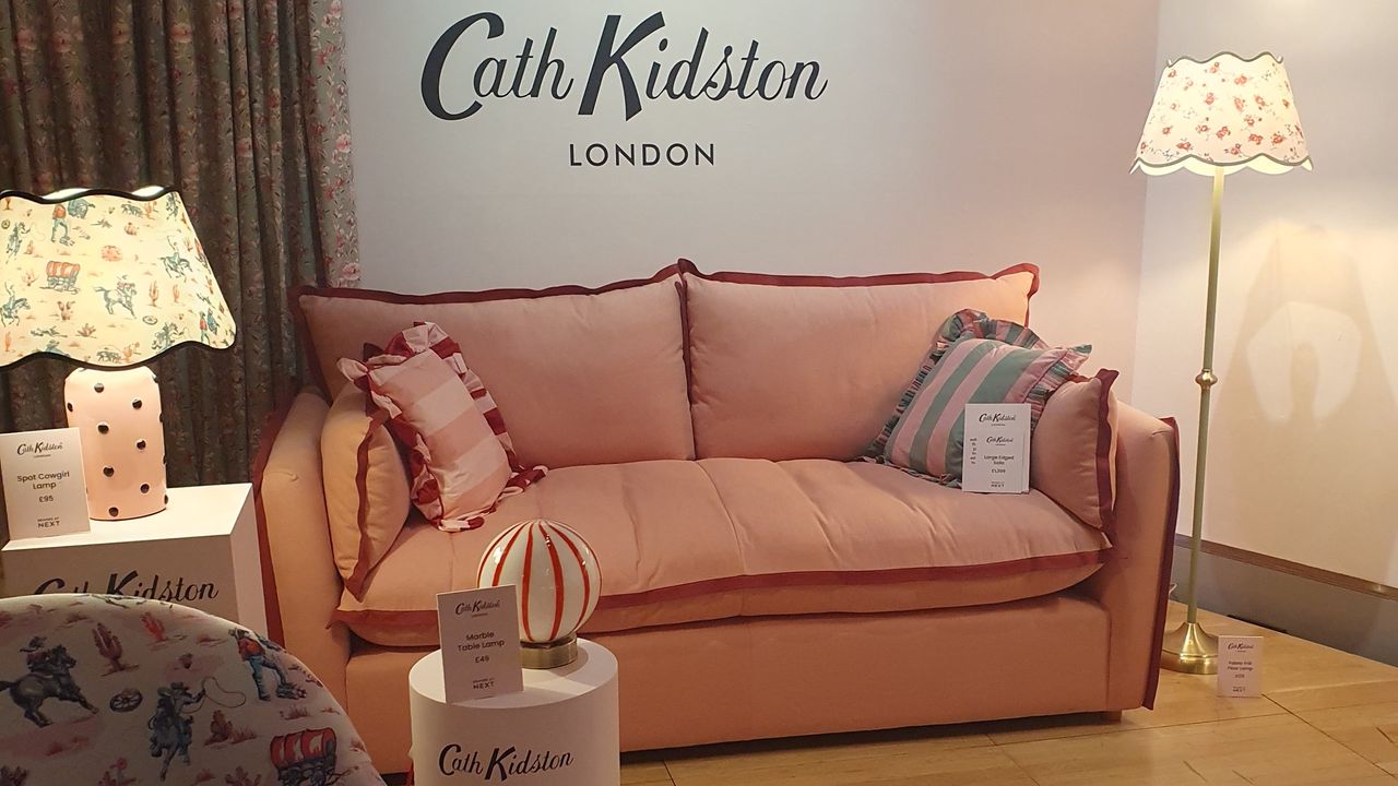 A pink sofa by Cath Kidston with two striped ruffled cushions on top and lamps with floral shades on either side