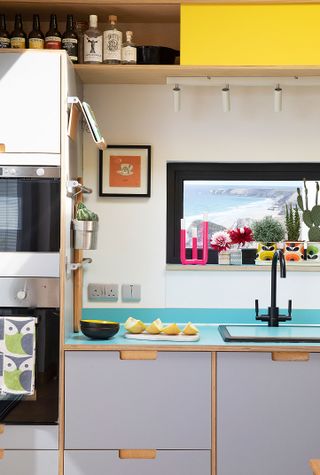 white plywood kitchen with blue splashback and colourful accessories