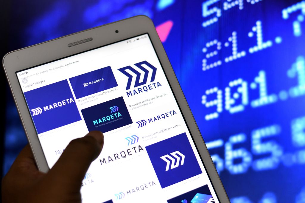 Marqeta logos seen displayed on an Android Tablet Phone with a ticker board in the background