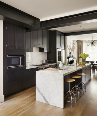 Kitchen color ideas featuring a black and white kitchen color scheme with black painted cabinetry, white marble island and wooden flooring.