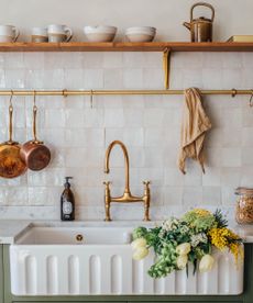 Cream tiled backsplash with fluted sink, golden tap and gold rail with copper pans