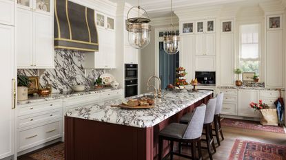 a white traditional kitchen with tall cabinetry, a statement marble countertop and splashback, a dark red island with marble and red vintage rugs