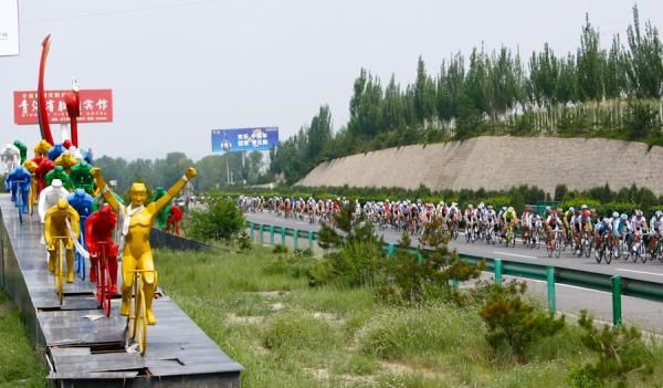 The peloton cruising along the cycling statue at Xidao Highway