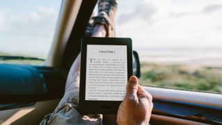 Someone reading a Kindle from the front seat of a car with their legs up