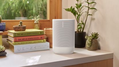 The Sonos Move 2 in white, on a shelf with some plants and books