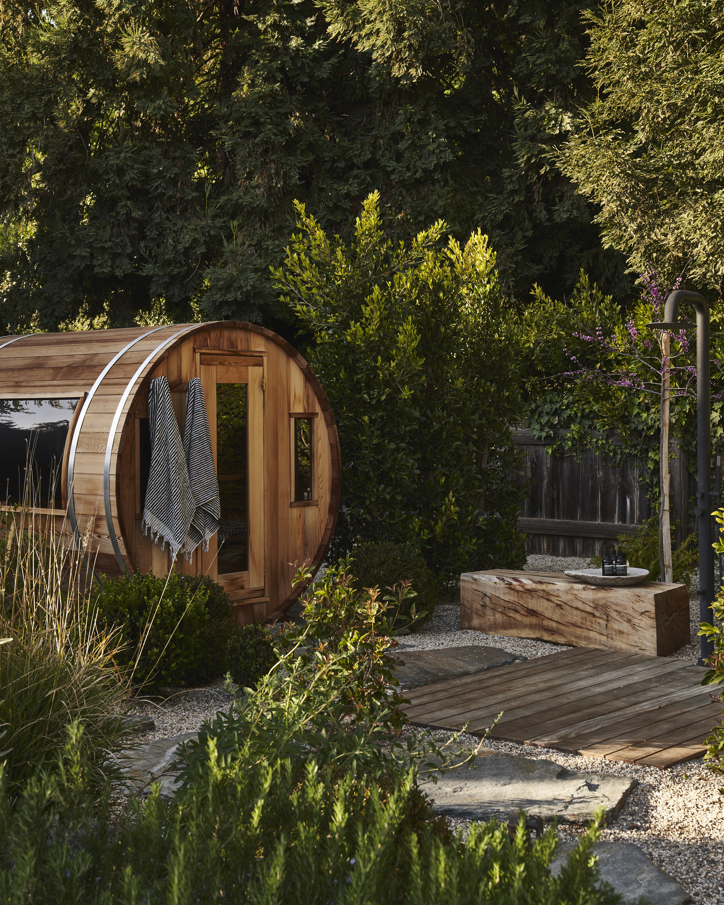 Wooden garden sauna with outdoor shower surrounded by planting and natural landscaping