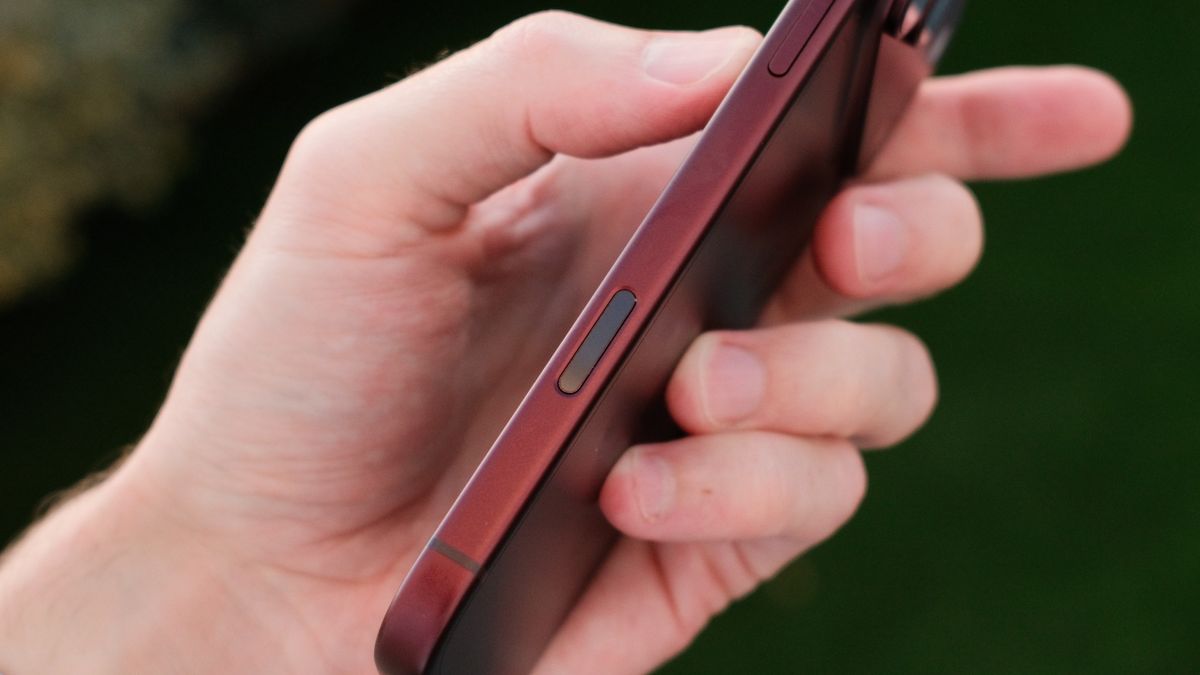 Close-up of the side of a burgundy iPhone 18 Pro Max showing a recessed control button while held in one hand.
