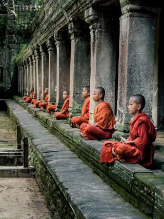 Young, shaven-headed Buddhist monks sitting by the side of a temple in contemplation