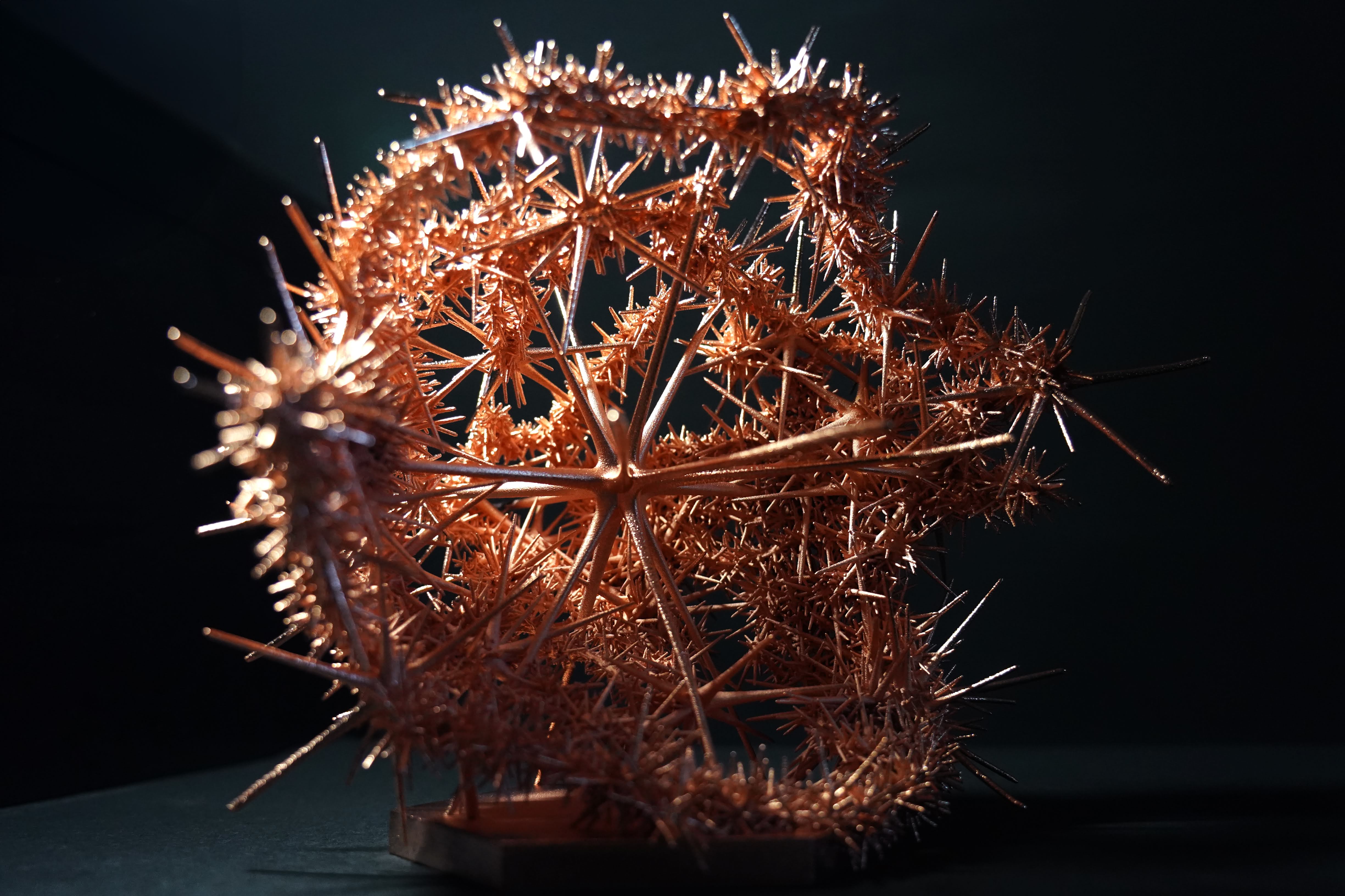 A spiky metal sculpture that is almost ball shaped in front of a dark background