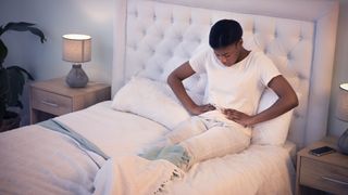 A woman clutches her belly in pain while sitting in bed