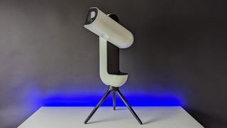 The Vaonis Vespera II smart telescope on a white tabletop with the optical tube assembly pointing upwards.