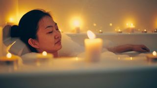 A woman relaxing with her eyes closed in a candlelit bath