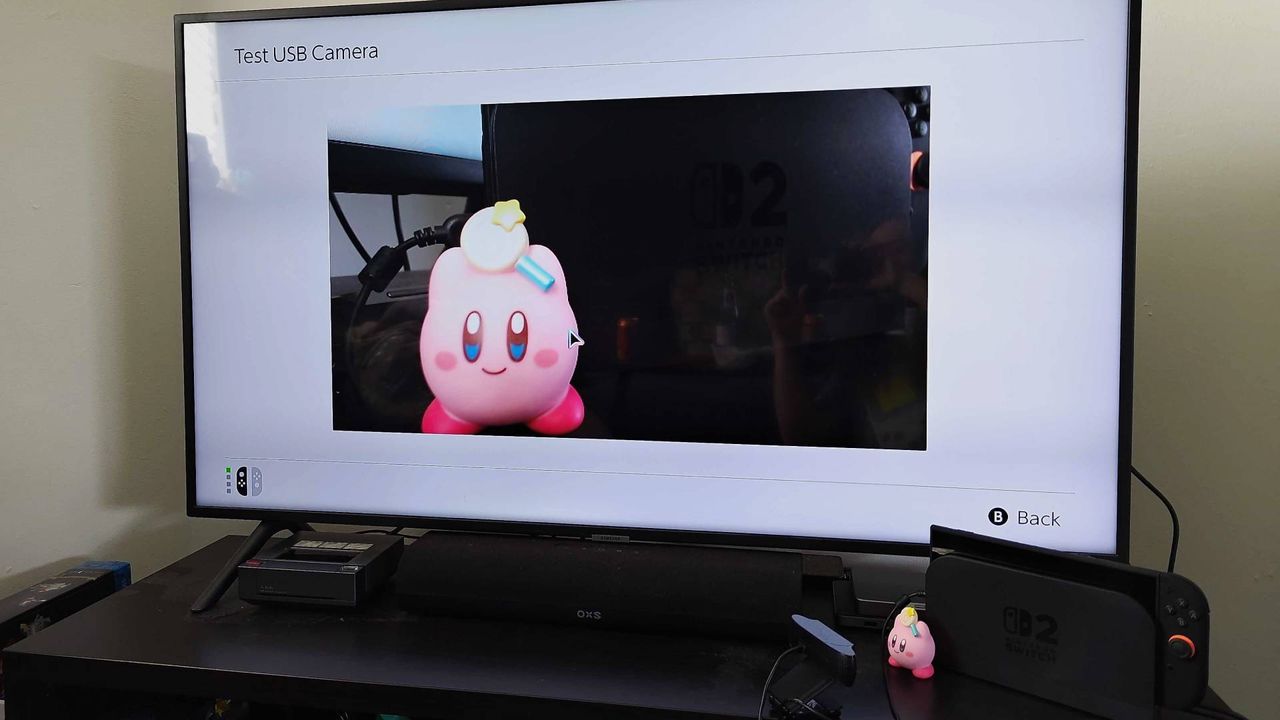 Switch 2 connected to dock and Samsung TV with Logitech webcam pointing at Kirby figure using Test USB Camera function.