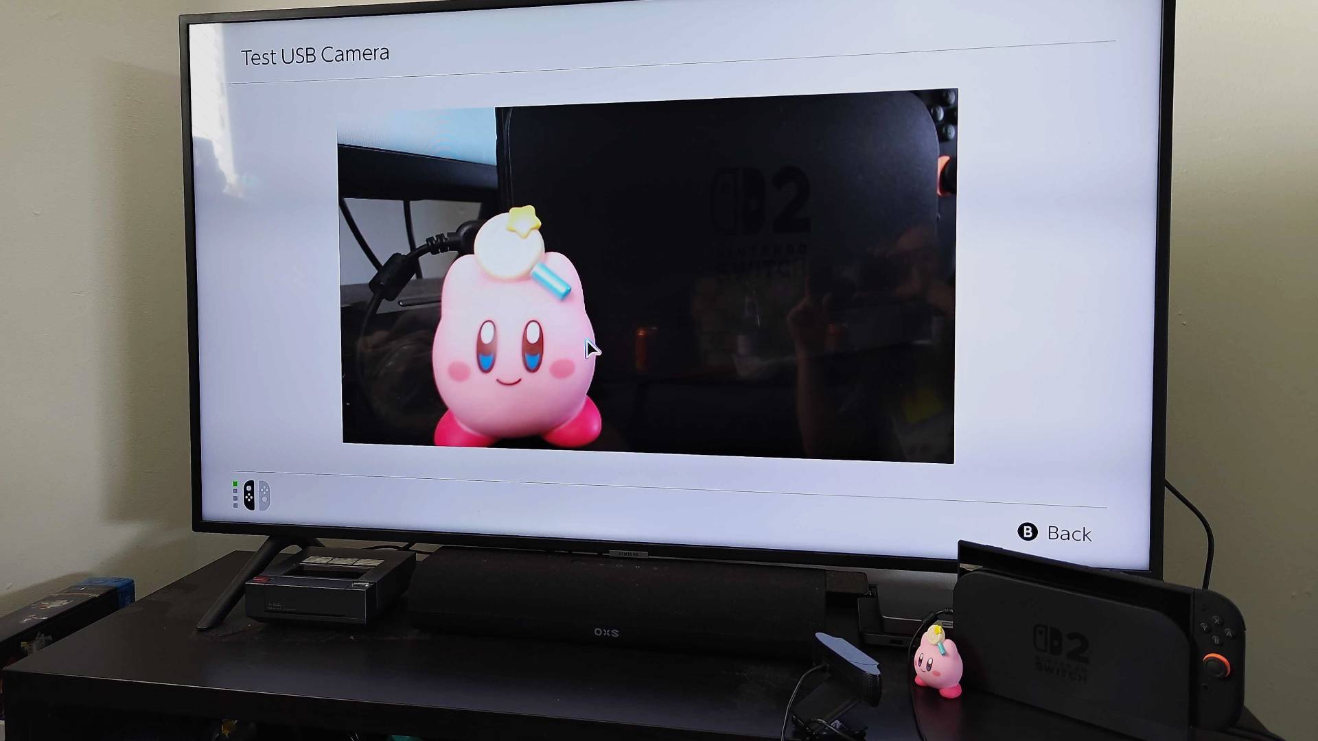 Switch 2 connected to dock and Samsung TV with Logitech webcam pointing at Kirby figure using Test USB Camera function.