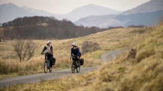 Jenny and a friend riding a road in Scotland