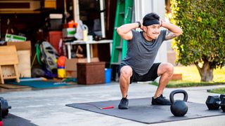 Man works out in front of his garage, performing unweighted squats. 