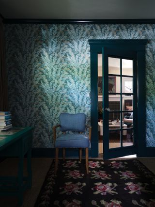 Room with green and blue patterned wallpaper, dark blue trim and dark floral rug
