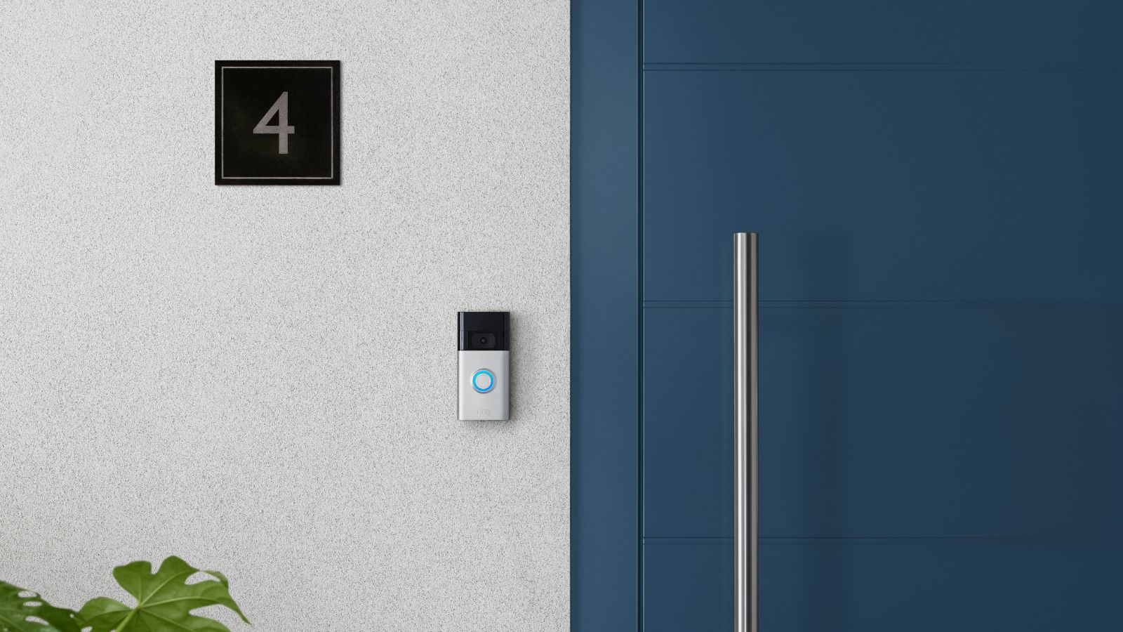 A second-generation ring camera doorbell mounted to a white wall beside a blue front door and a 'number 4' plate.