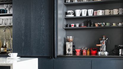 White kitchen with wooden shelves filled with mugs, and a red coffee machine on a white worktop