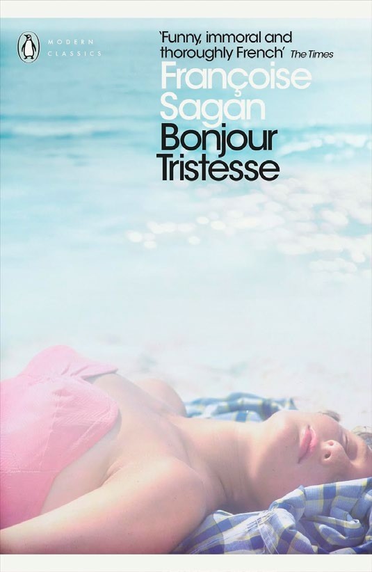 A woman lying on a beach, sunbathing, with the book cover of 'Bonjour Tristesse' by Françoise Sagan prominently displayed.