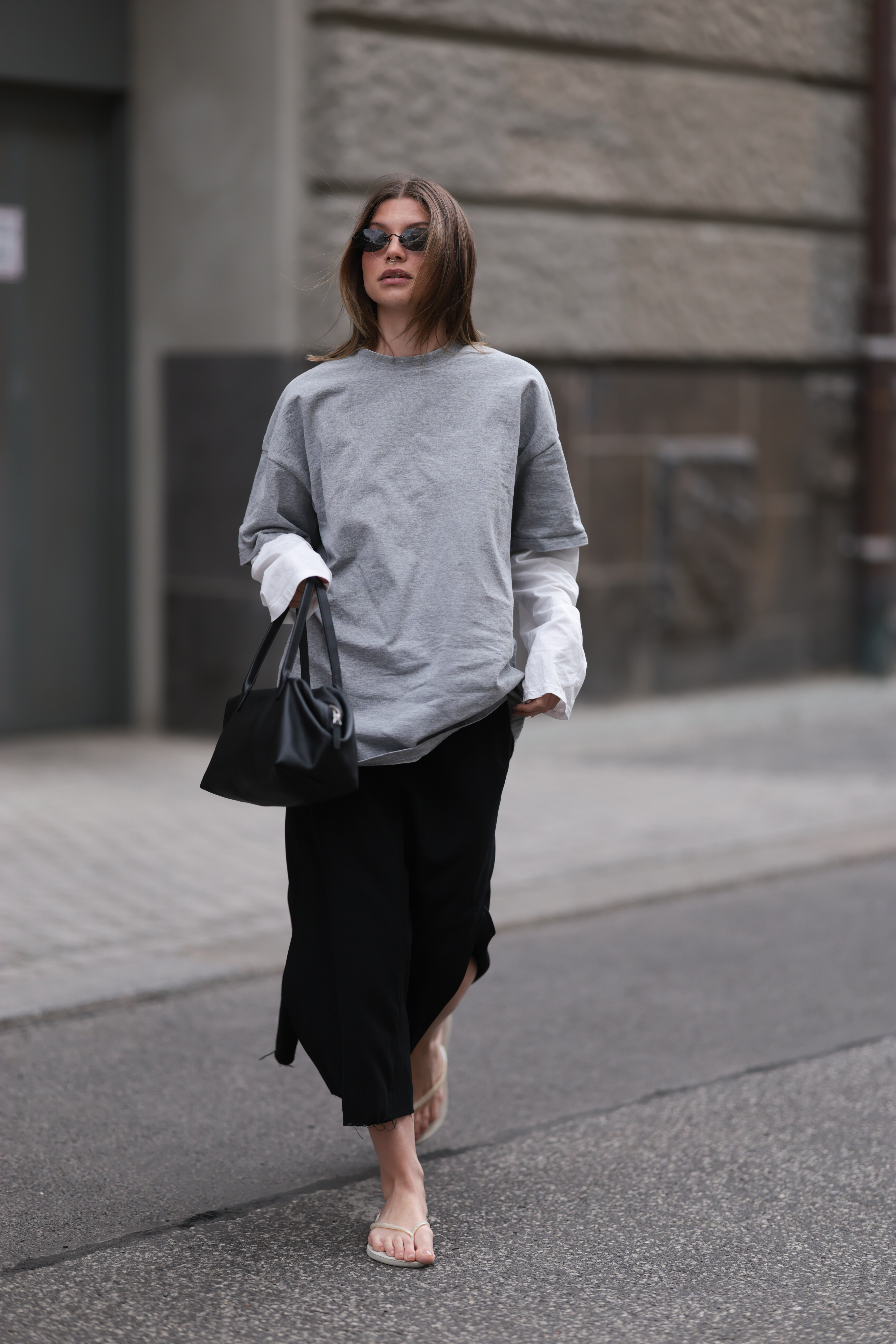 Sophia Geiss seen wearing an oversized grey Jil Sander shirt, white long sleeve top, black COS midi skirt, black COS bag, Vehla Eyewear sunglasses, light Havaianas flip flops.