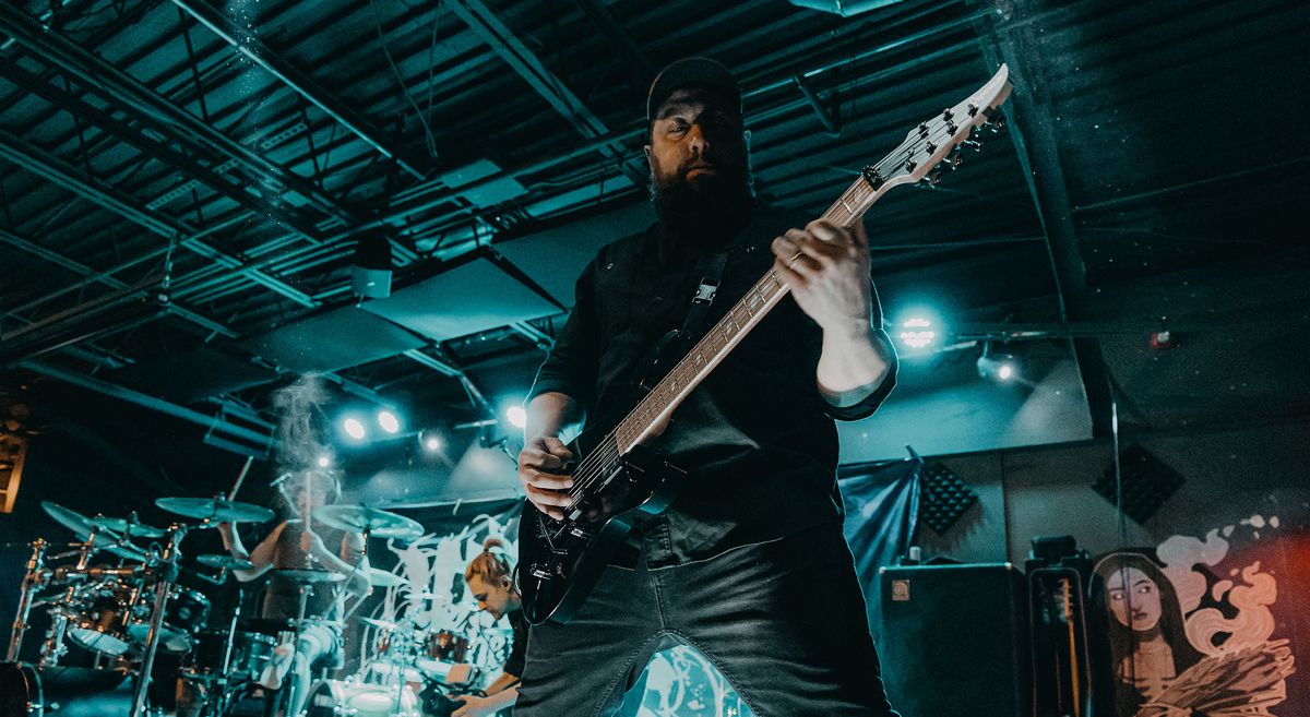 Within the Ruins&#039; Joe Cocchi wears a ballcap and riffs on his 7-string Caparison live onstage,with steely blue-green stagelights behind him.