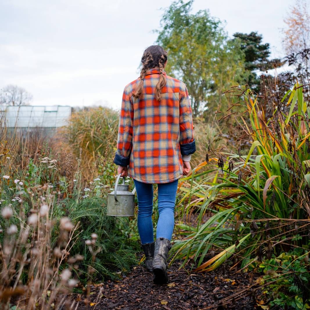 The back of a woman in flannel walking through a garden in fall