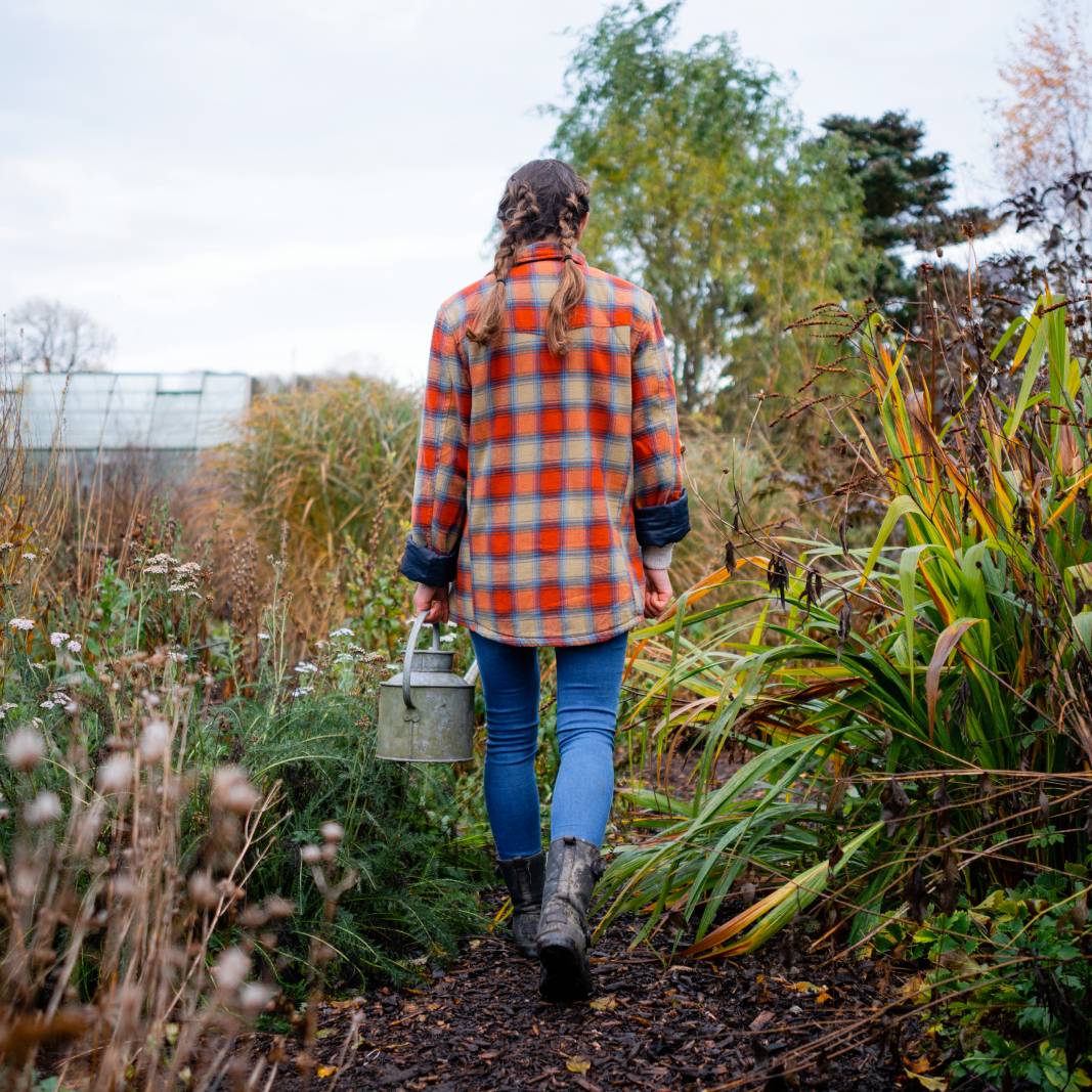 The back of a woman in flannel walking through a garden in fall